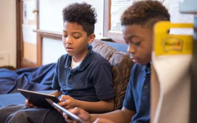 Two students sit on couch, reading from tablets