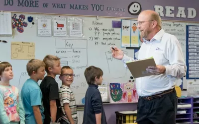 Students stand in line in front of teacher while he holds notebook, speaking