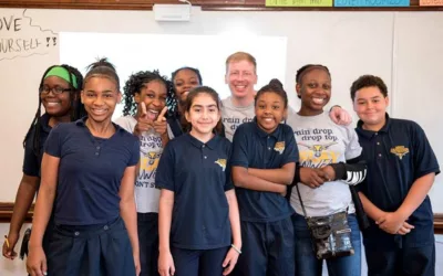 Eight students stand with teacher in front of white board, smiling