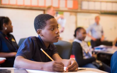 Student sits in classroom, looking off to the side as he holds a pencil