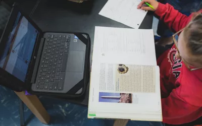 Overhead view of student studying from book, in front of laptop