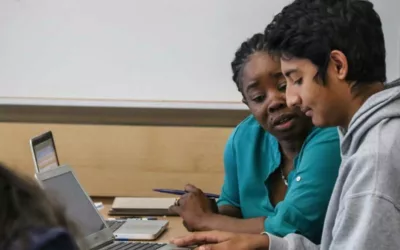 Photo of student and teacher working together seated at a table in front of a laptop