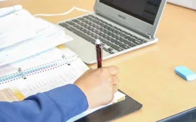 Photo of student arm writing in notebook with laptop in background