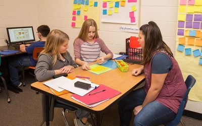 Teacher works with pair of students at small desk