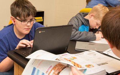 Student looks closely at laptop while other students work around him