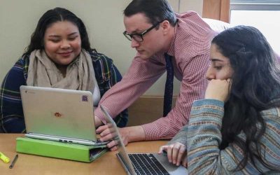 Photo of teacher working with two students on their laptops
