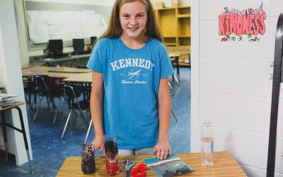 Student smiles for photo, standing in front of table with experiment materials