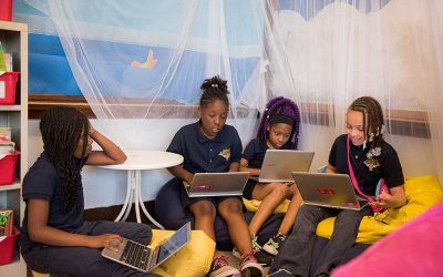 Four female students sit on floor, bean bag chairs while working on laptops