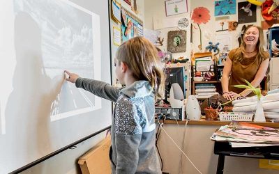 Female student points at white board while teacher looks on, smiling