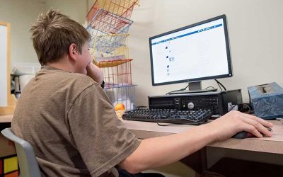 Student sits with hand on computer mouse while looking at computer screen