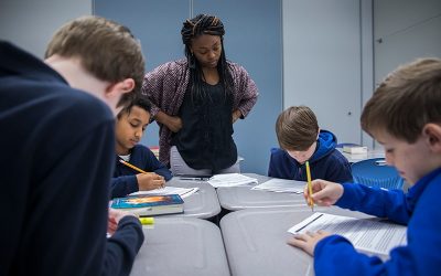 Teacher looks on as students complete work at desk