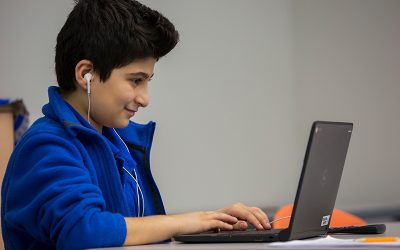 Student wearing earphones smiles as he works on laptop