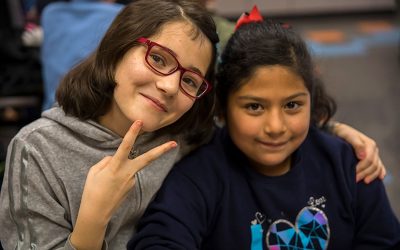 Two students, one showing a peace sign, draping her arm around another student's shoulders