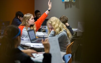 Student raises her hand, sitting among classmates