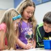 Three elementary students working together at table with several resources