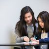 Two students working together at desk, looking on together at paper