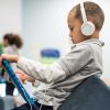 Young student wears headphones and looks down at tablet he is holding