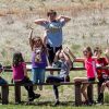 Students sit, smiling, at outdoor picnic table with arms raised in the air